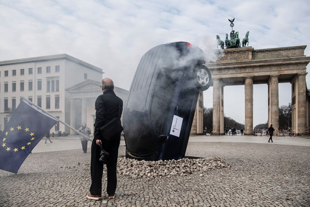 Ein SUV steckt scheinbar im Boden vor dem Brandenburger Tor, aus dem Heckbereich steigt Qualm.