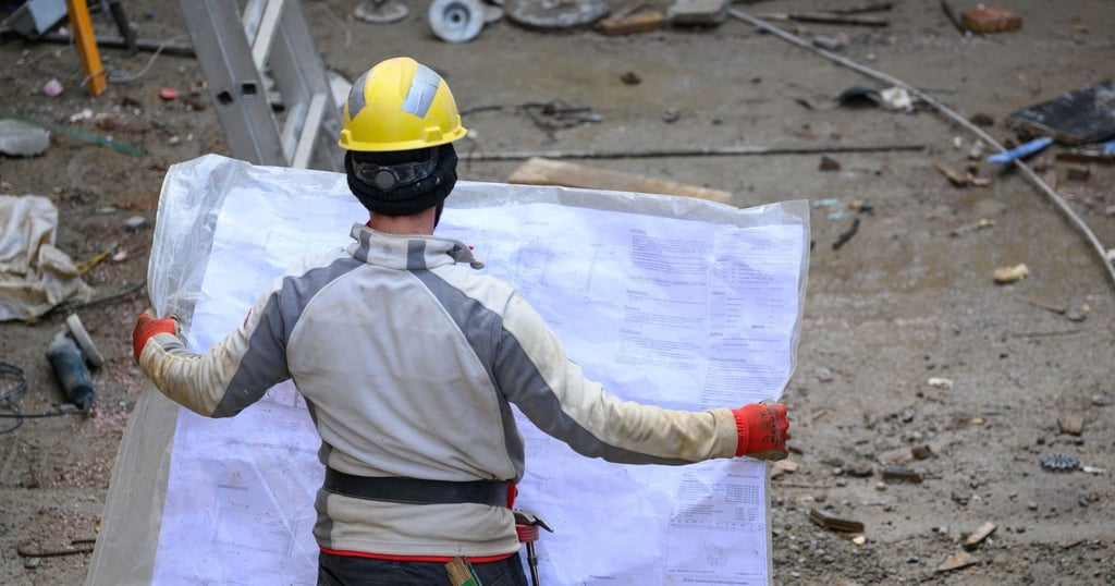 Ein Bauarbeiter schaut auf der Baustelle des Anbaus am Firmensitz der Carl Zeiss Digital Innovation GmbH am Fritz-Foerster-Platz in einen Bauplan.
