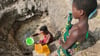Eine Frau schöpft in Mosambik Wasser aus einer ungeschützten Quelle.
