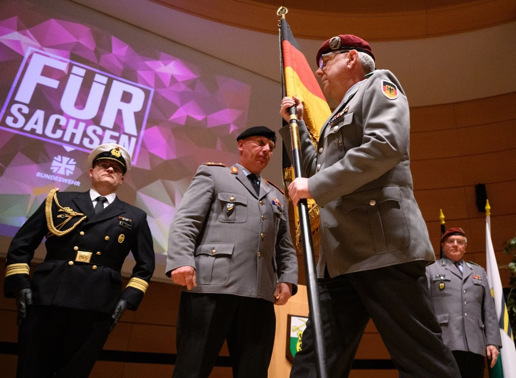 Generalmajor Andreas Henne (M) übergibt die Truppenfahne an den neuen Kommandeur Oberst Michael H. Popielas (3.v.l.).