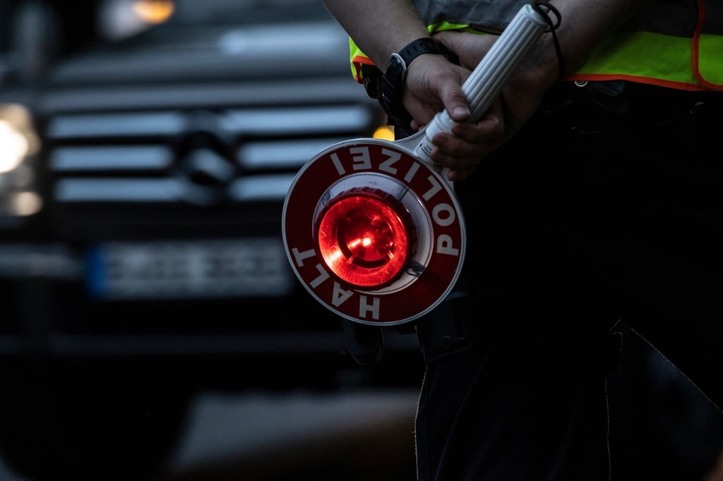 Ein Polizist hält bei einer Verkehrskontrolle eine Winkerkelle in der Hand.