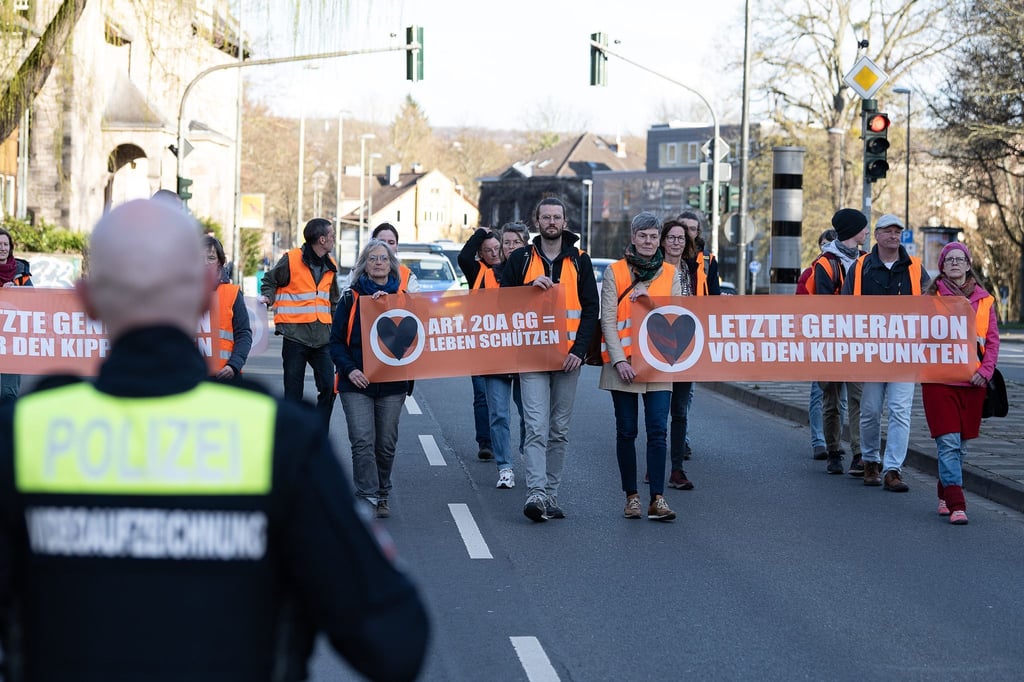 Aktivisten der Bewegung „Letzte Generation“ gehen mit Plakaten bei einem friedlichen Protestmarsch über eine Hauptverkehrsstraße.