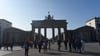 Touristen stehen vor dem Brandenburger Tor in Berlin.