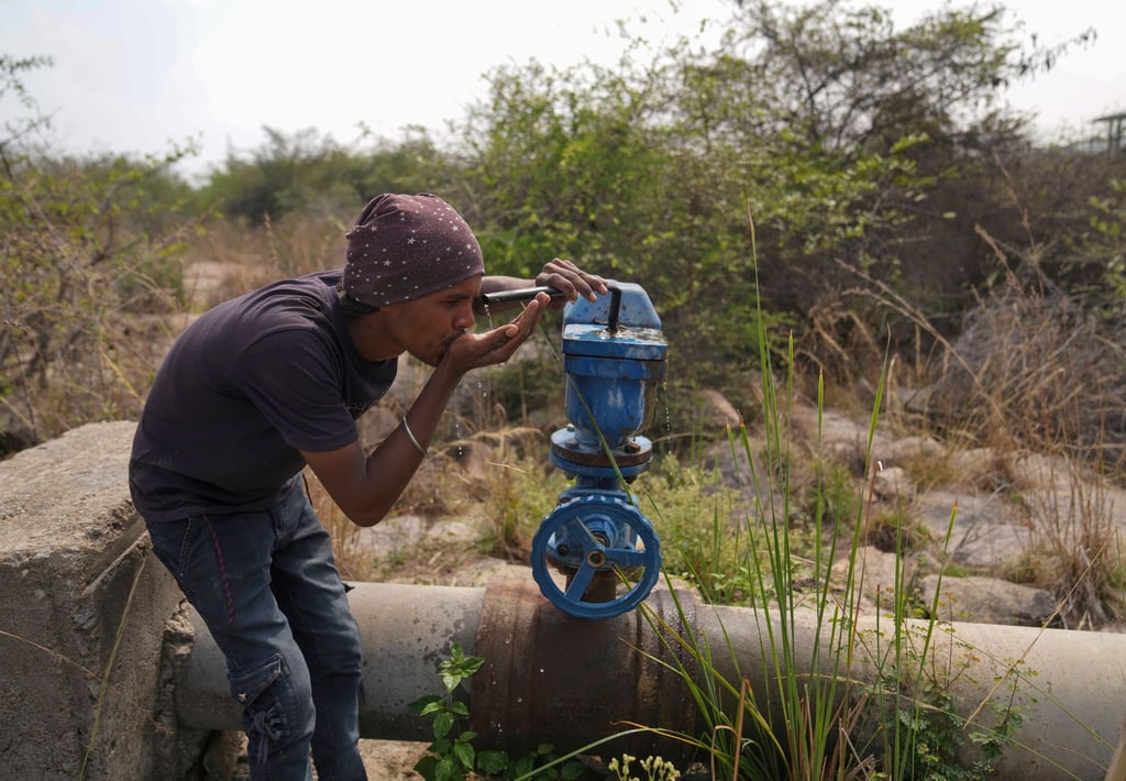 In Indien trinkt ein Mann Wasser aus einer undichten Wasserstelle.
