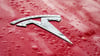 Das Logo auf der nassen Motorhaube eines roten Tesla.