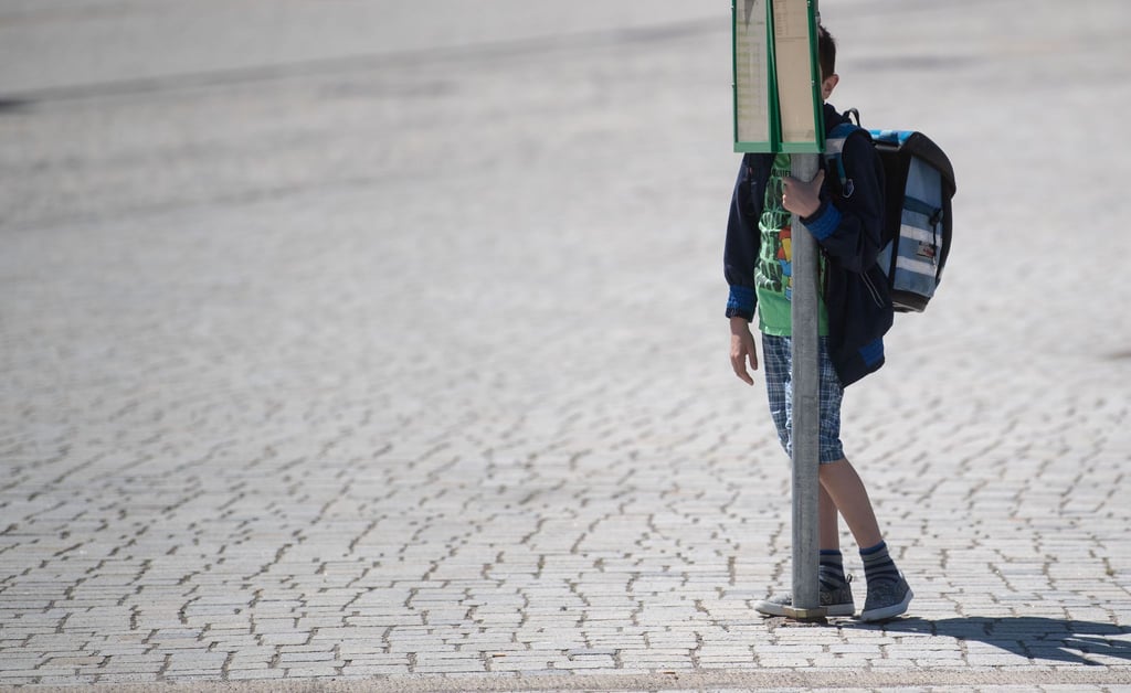 Ein Schüler steht an einem Pfahl mit Fahrplan an einer Bushaltestelle in der Innenstadt.