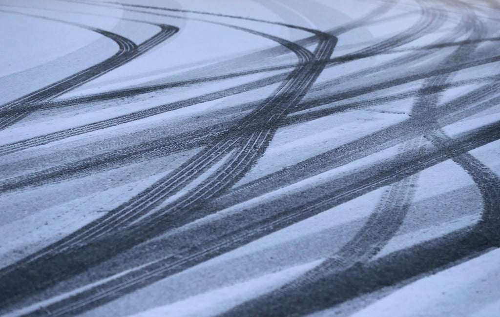 Reifenspuren zeichnen sich auf einer Straße im Schnee ab.