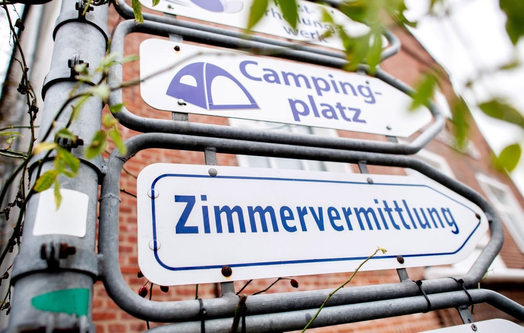 Schilder mit den Aufschriften „Campingplatz“ und „Zimmervermittlung“ hängen an einer Kreuzung.