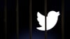 Das Twitter-Logo auf einem Bildschirm hinter Gittern.
