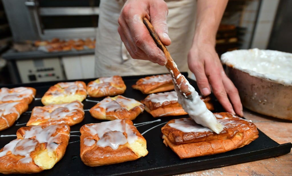 Ein Bäckermeister pinselt Zuckerguss auf süßes Gebäck in seiner Backstube.