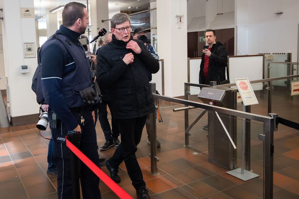 Kardinal Rainer Maria Woelki wird im Foyer des Kölner Landgerichts von einem Justizbeamten (l) zur Sicherheitsschleuse begleitet.