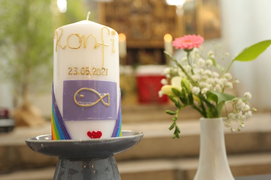 Eine Konfirmationskerze und Blumen stehen in einer Kirche.