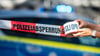 Ein Absperrband wird vor einem Polizeiwagen ausgerollt.