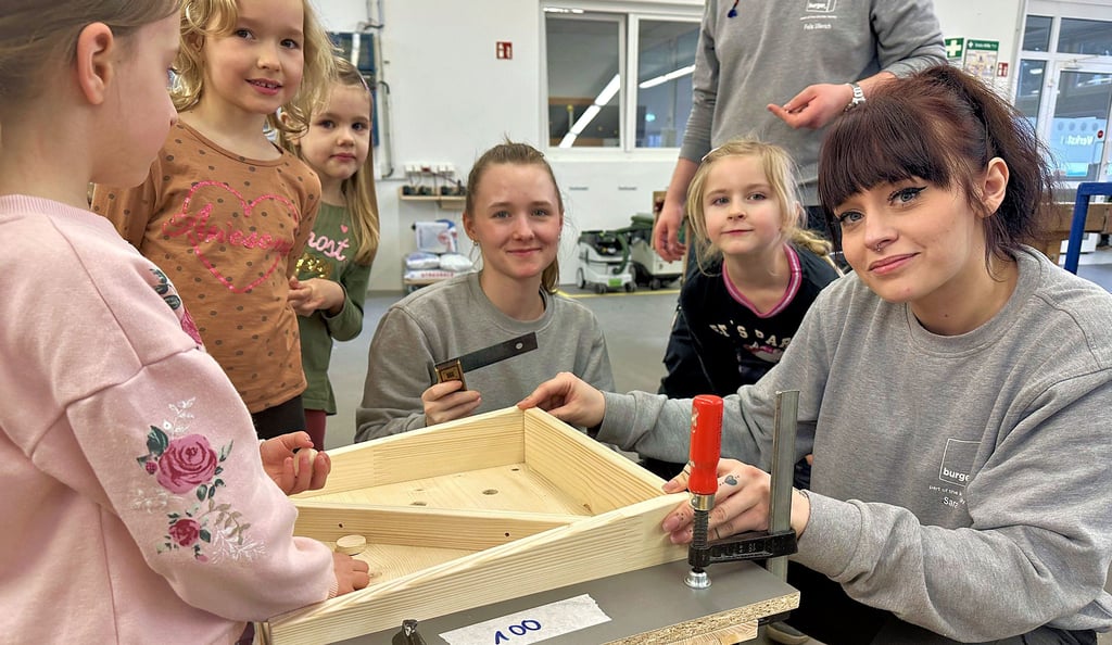 Gemeinsam mit Holz arbeiten: Die Jungen und Mädchen der Burger Kindertagesstätte „Bambi“ haben mit Sarah Abe (r.) und Samantha-Nadine Krause in der Lehrlingswerkstatt der Burger Küchenmöbel GmbH ihren Spaß.
