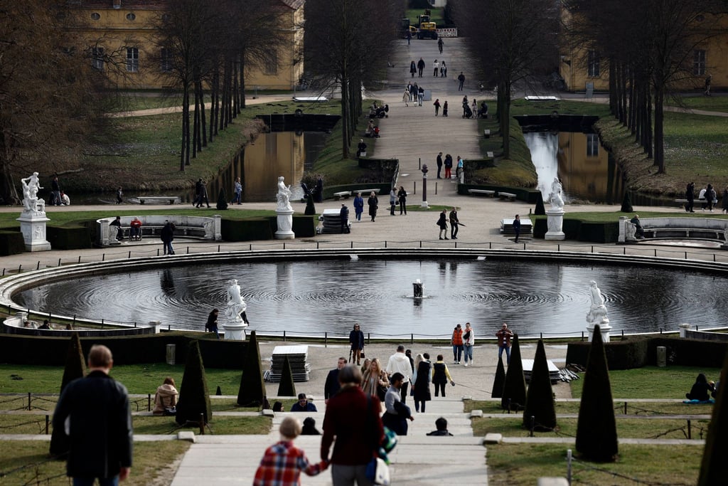 Passanten gehen bei sonnigem Wetter auf den Terrassen von Schloss Sanssouci spazieren.