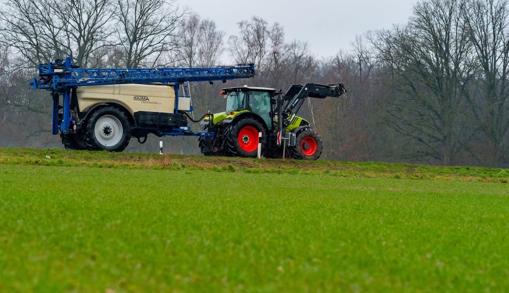 Ein Landwirt fährt mit seinem Trecker samt angehängter Spritze über eine Straße.