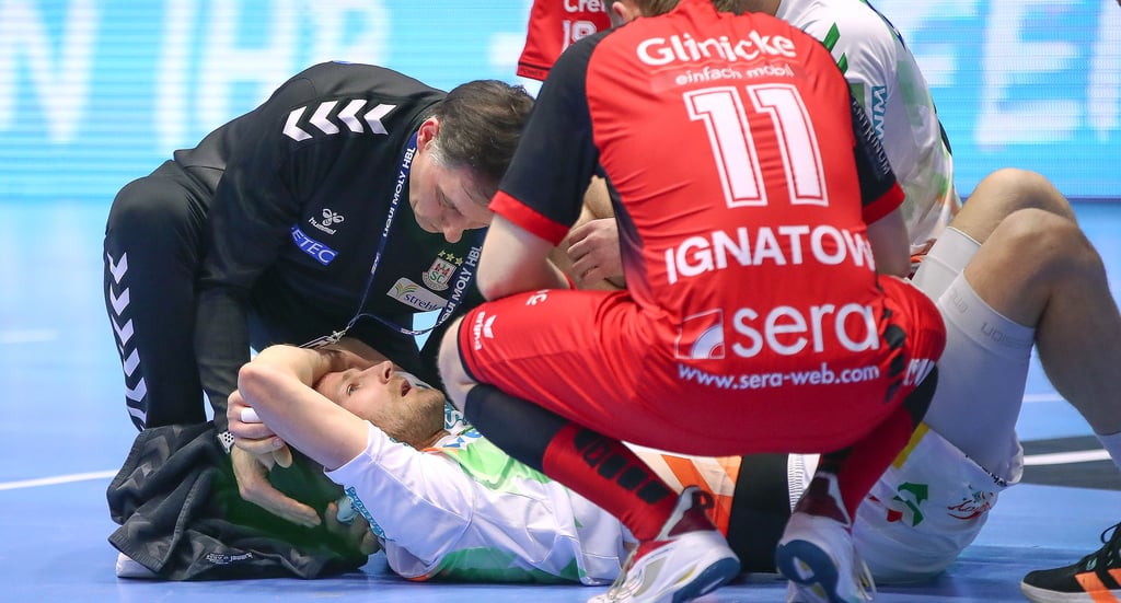 Sichtlich benommen liegt Magdeburgs Rückraumspieler Philipp Weber nach dem harten Aufprall am Boden und wird von SCM-Physiotherapeut Andreas Grote behandelt. Auch der Melsungener Dimitri Ignatow will helfen.