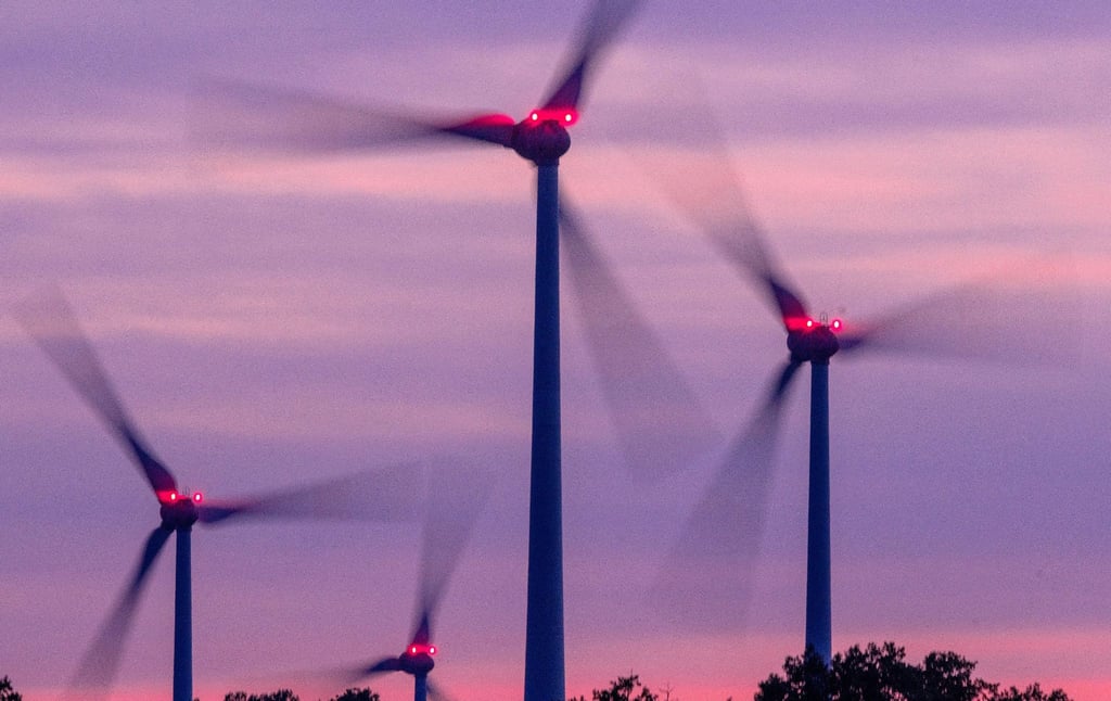 Mit Signallampen beleuchtete Windräder drehen sich nach Sonnenuntergang.