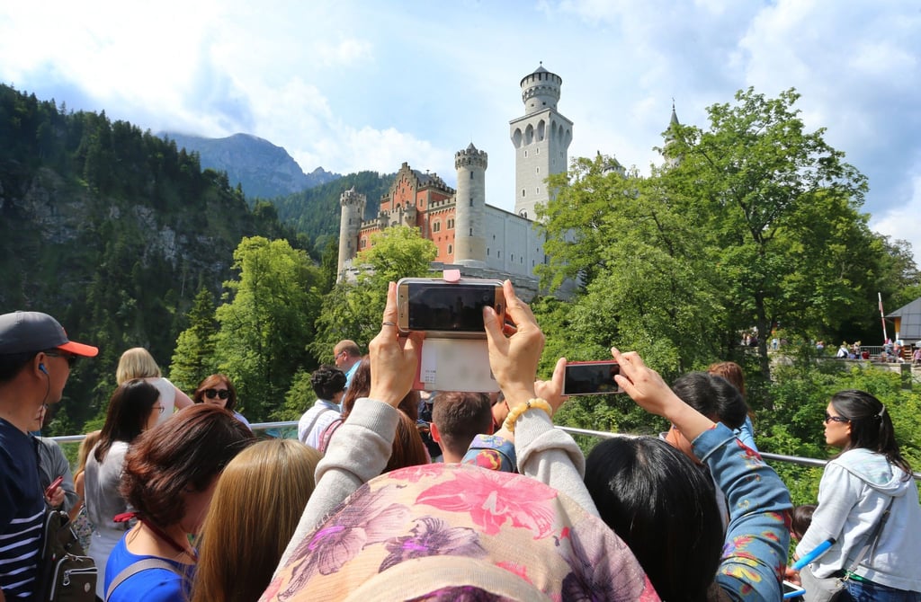Touristen stehen auf einer Aussichtsplattform unterhalb des Schlosses Neuschwanstein.