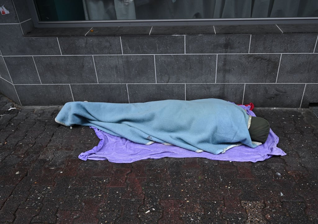 Eine obdachlose Person schläft auf einem Gehweg.