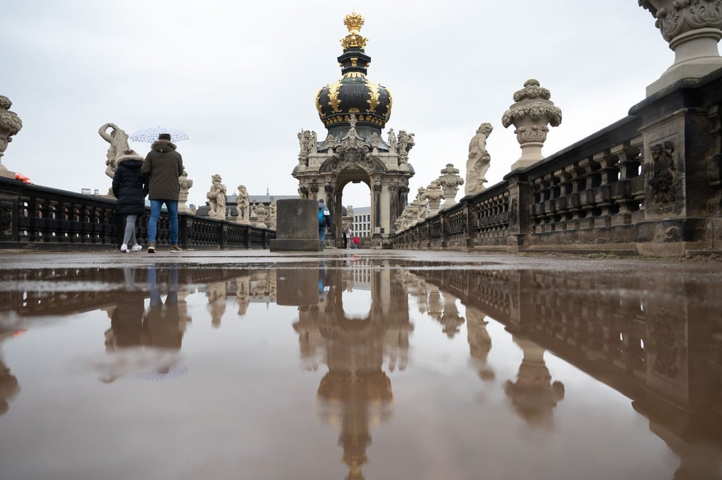 Passanten spiegeln sich in einer Pfütze vor dem Kronentor im Dresdner Zwinger.