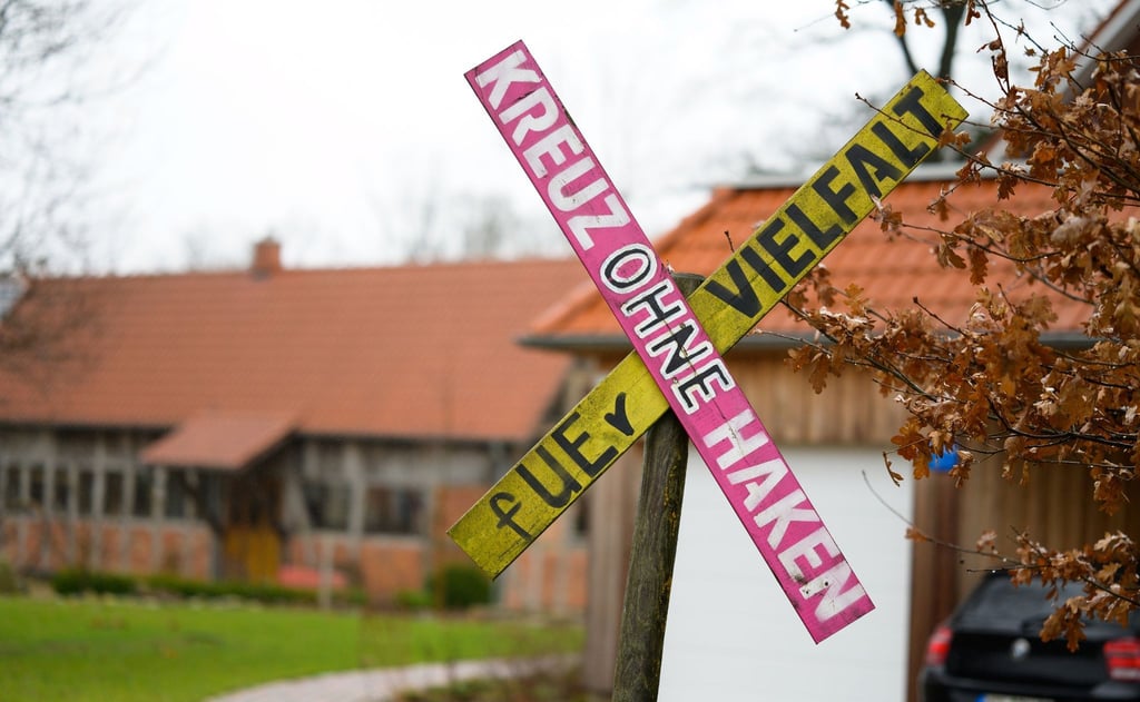 Ein Holzkreuz mit der Aufschrift „ Kreuz ohne Haken fUEr Vielfalt“ steht an einer Hofeinfahrt.