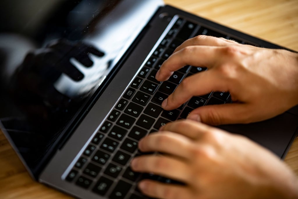 Ein Mann tippt auf einer Tastatur eines Laptops.