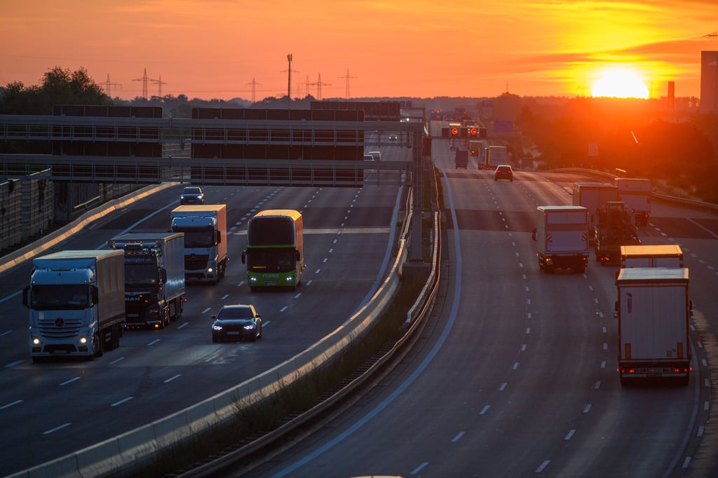 Lastwagen und Autos rollen bei Sonnenaufgang auf der Autobahn A2 an Magdeburg vorbei.