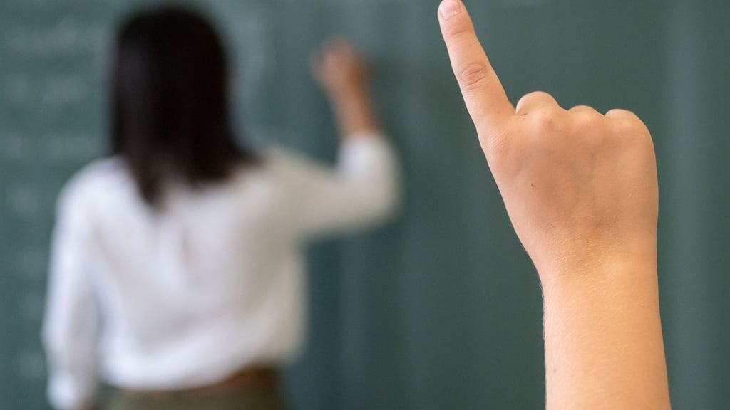 Ein Schüler meldet sich, während die Lehrerin an die Tafel schreibt.
