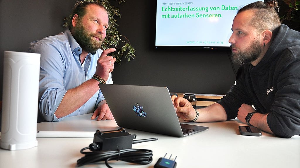 Florian Lühr (links) und Martin Mertens vom Stendaler Start-up Our-Green erklären, was mit ihren Sensoren möglich ist. Im Vordergrund ist ein gewöhnlicher Bodenfeuchtigkeitsmesser zu sehen.