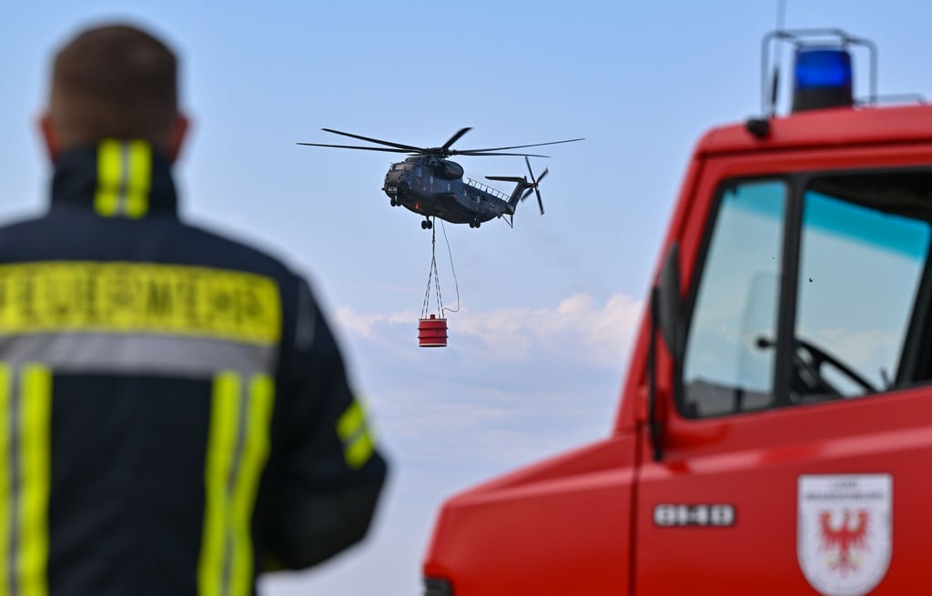 Ein Hubschrauber der Luftwaffe fliegt mit einem Wasserbehälter während einer Übung in Müncheberg.