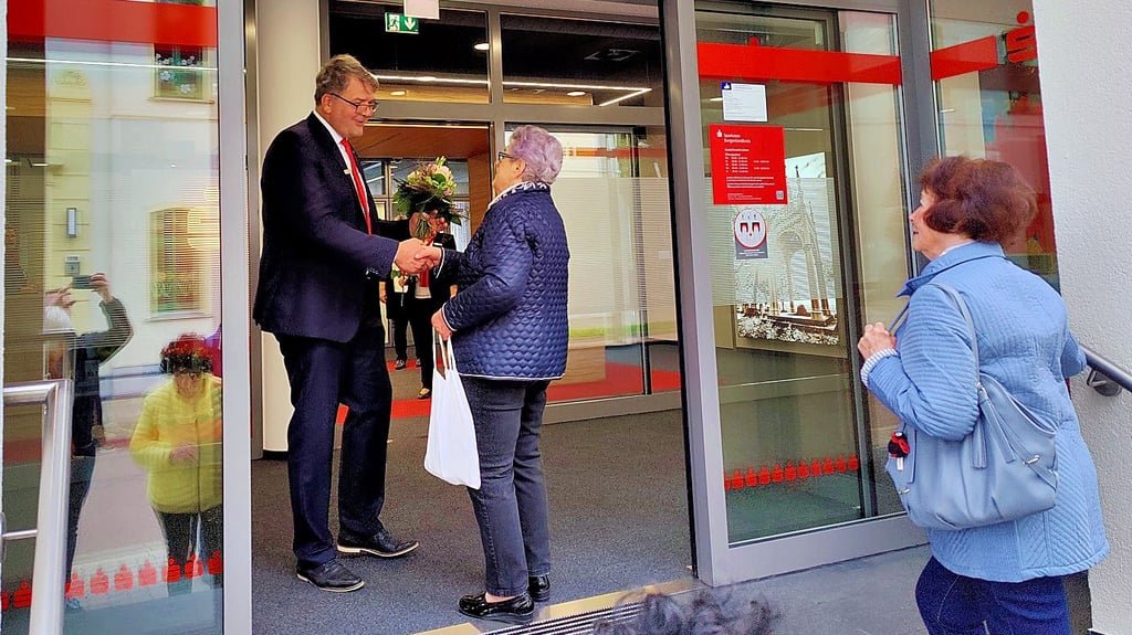 Sparkasse in Lützen ist wieder offen: Jörn Stauch vom Sparkassen-Vorstand im Burgenlandkreis begrüßt die erste Kundin der sanierten Geschäftsstelle mit einem Blumenstrauß.