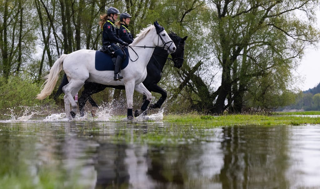 Die Polizeireiterin Lisa-Marie Schulz (l) und Anna Hartmann reiten mit ihren Dienstpferden am Ufer der Elbe entlang.