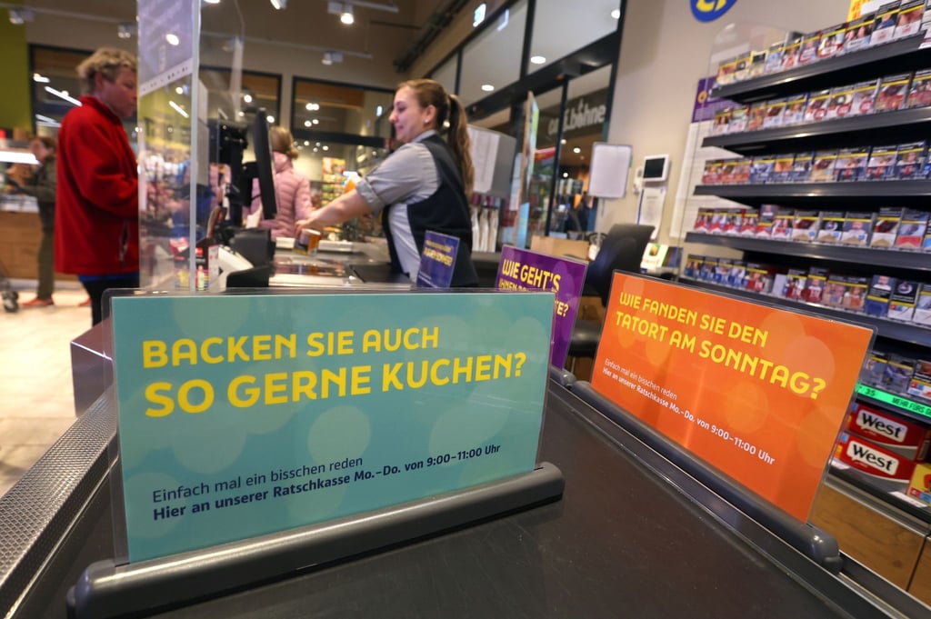 Eine Kassiererin steht mit einem Kunden bei der Eröffnung einer „Ratschkasse“ (Plauderkasse) in einem Edeka-Markt in Buxheim.