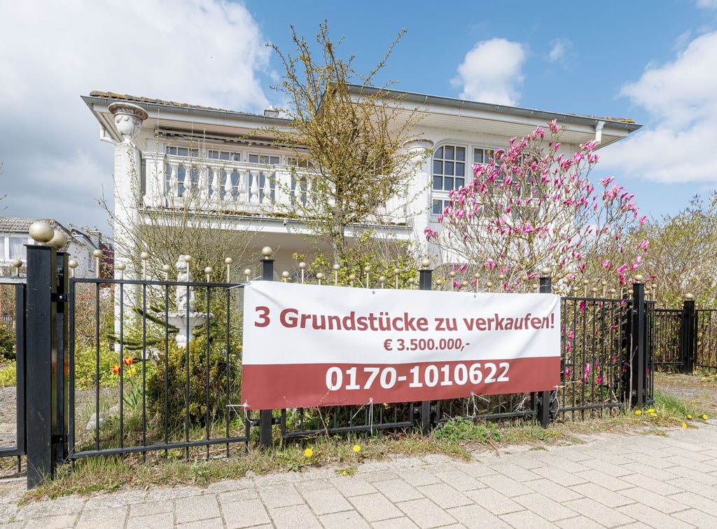 Ein Transparent mit der Aufschrift „3 Grundstücke zu verkaufen! €3.500.000“ hängt an einem Grundstück.