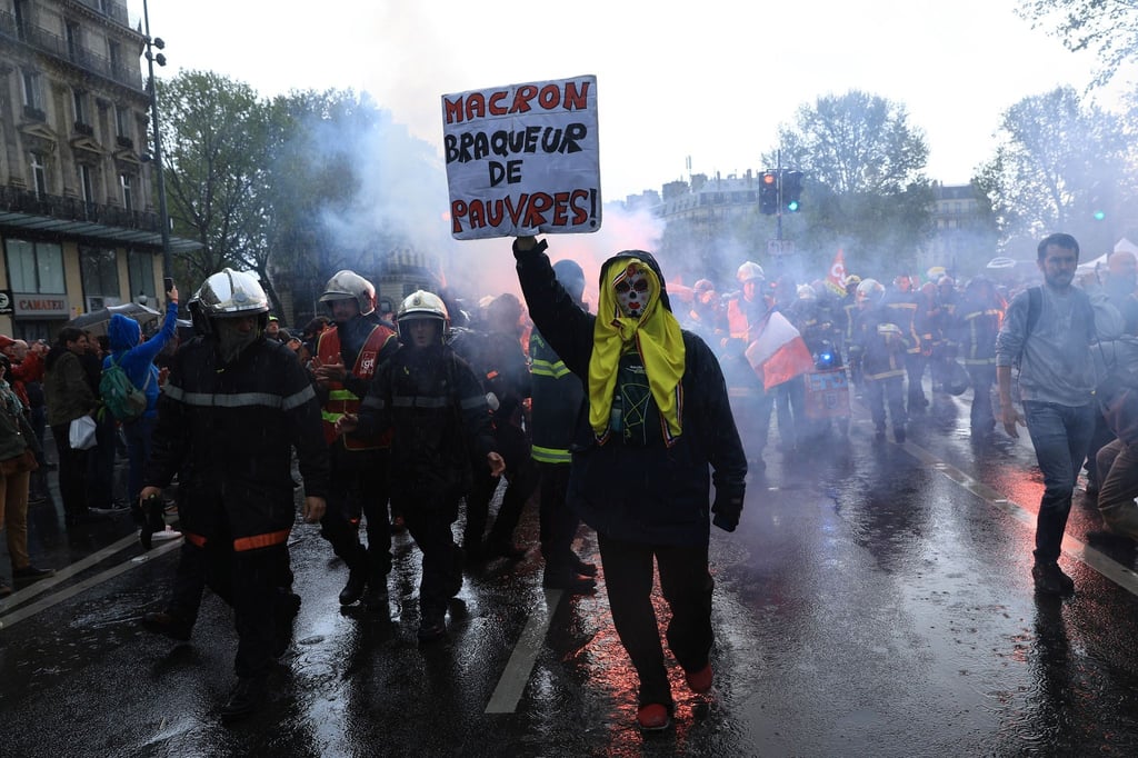 Rettungskräfte und ein Demonstrant mit einem Plakat mit der Aufschrift „Macron, Räuber der Armen“ marschieren während einer Demonstration anlässlich des Tages der Arbeit in Paris.
