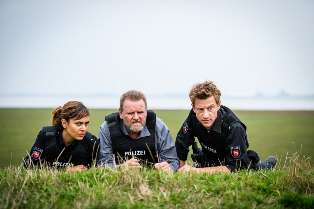 Süher Özlügül (Sophie Dal, l.), Kriminalhauptkommissar Brockhorst (Felix Vörtler, M.) und Henk Cassens (Maxim Mehmet, r.) beobachten eine Situation vom Deich aus.