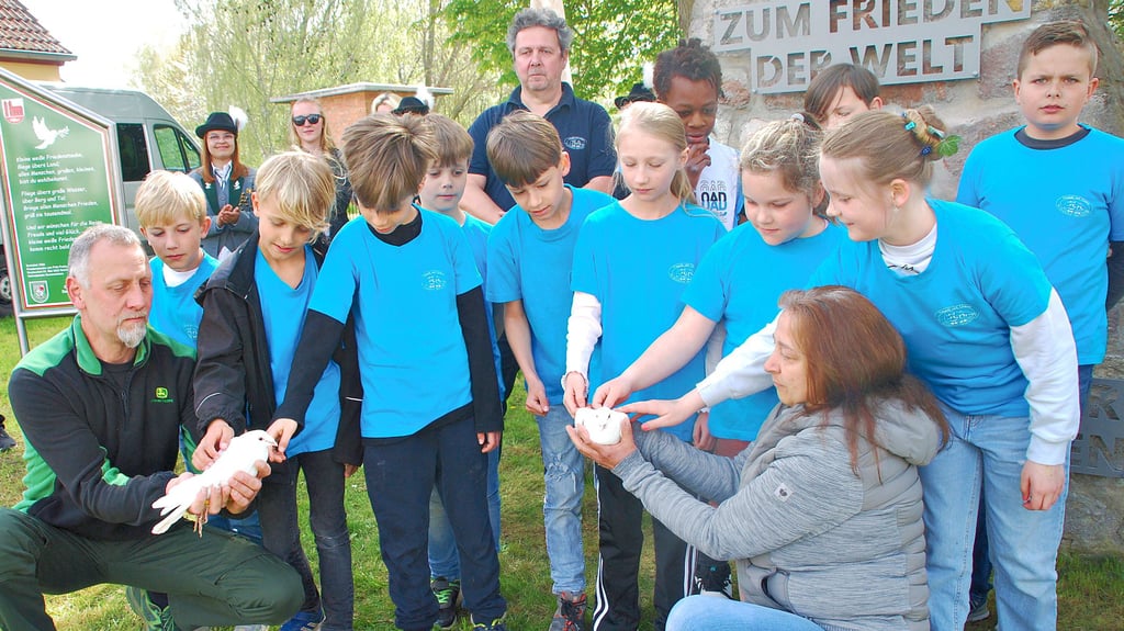 Die Kinder der Grundschule „Martin Selber“ streicheln die beiden weiße Friedenstauben, die Thomas und Ute Speckhals, die in der Domersleber Friedensstraße wohnen, symbolisch aufsteigen ließen.