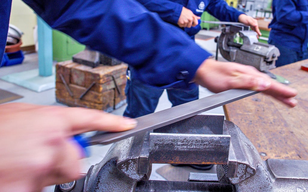 Lehrlinge arbeiten mit der Metallfeile an Schraubstöcken in einer Lehrwerkstatt.