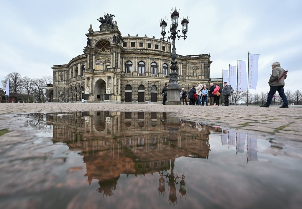 Die Semperoper spiegelt sich in einer Pfütze auf dem Theaterplatz.