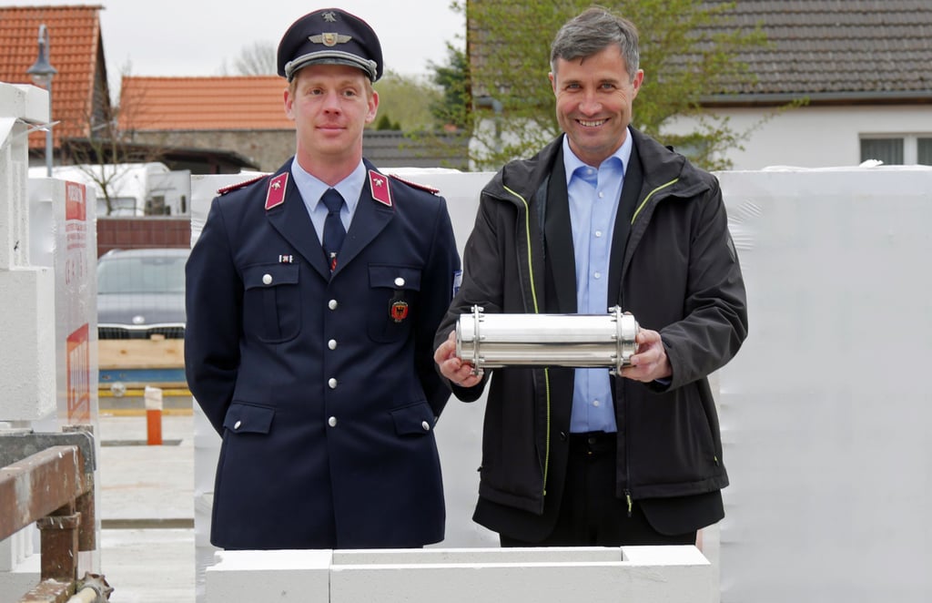 Wehrleiter Enrico Hahn (l.) und Bürgermeister Carsten Miehe versenken die Zeitkapsel im Rohbau des neuen Feuerwehrgerätehauses.