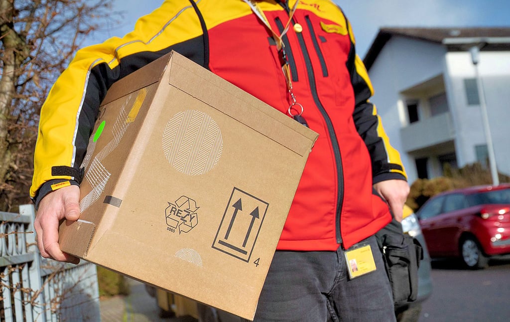 Ein DHL-Mitarbeiter trägt ein Paket unter seinem Arm. Die Rückgabe nicht bestellter Päckchen kann mit Bürokratie und Kosten verbunden sein.