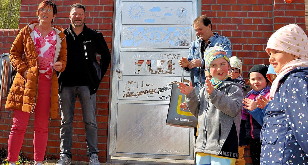 Kita-Leiterin Kerstin Martin, und Roman Giebel, stellvertretender Produktionsleiter bei Lampe, und Konstrukteur Frank Arandt stellen mit den Kita-Kindern das neue Eingangstor vor.
