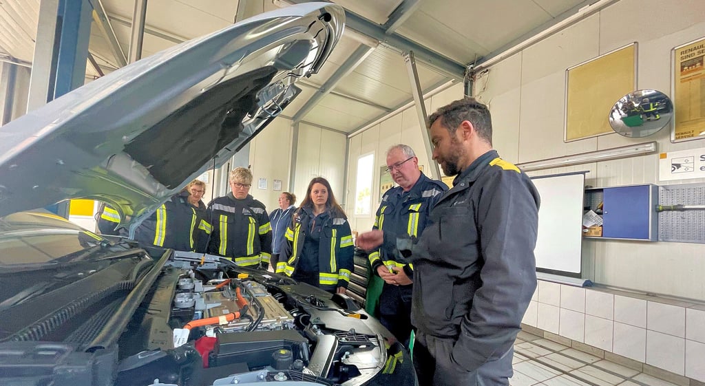 Autohausmitarbeiter Alexander Hanisch zeigt Wehrleiter Jörg Hohmann, Sina Meinhardt sowie Viktoria Luise und Paula Hohmann von der Hüttenröder Feuerwehr, wie ein E-Auto aufgebaut ist.
