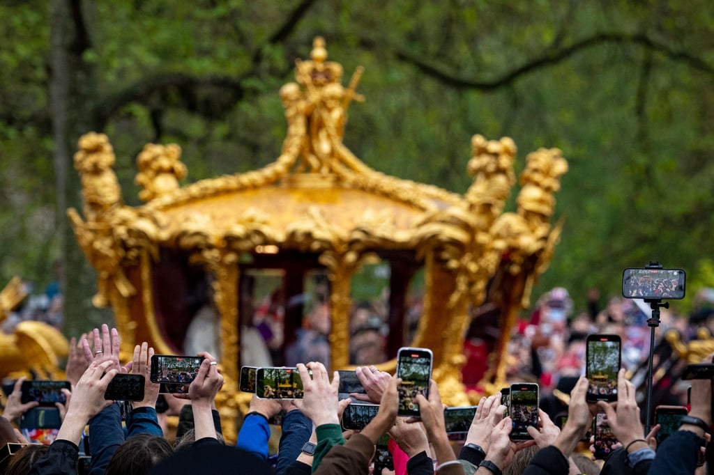Menschen filmen den britischen König Charles III. und Königin Camilla in der goldenen Staatskutsche auf dem Rückweg von der Krönungszeremonie zum Buckingham Palast.