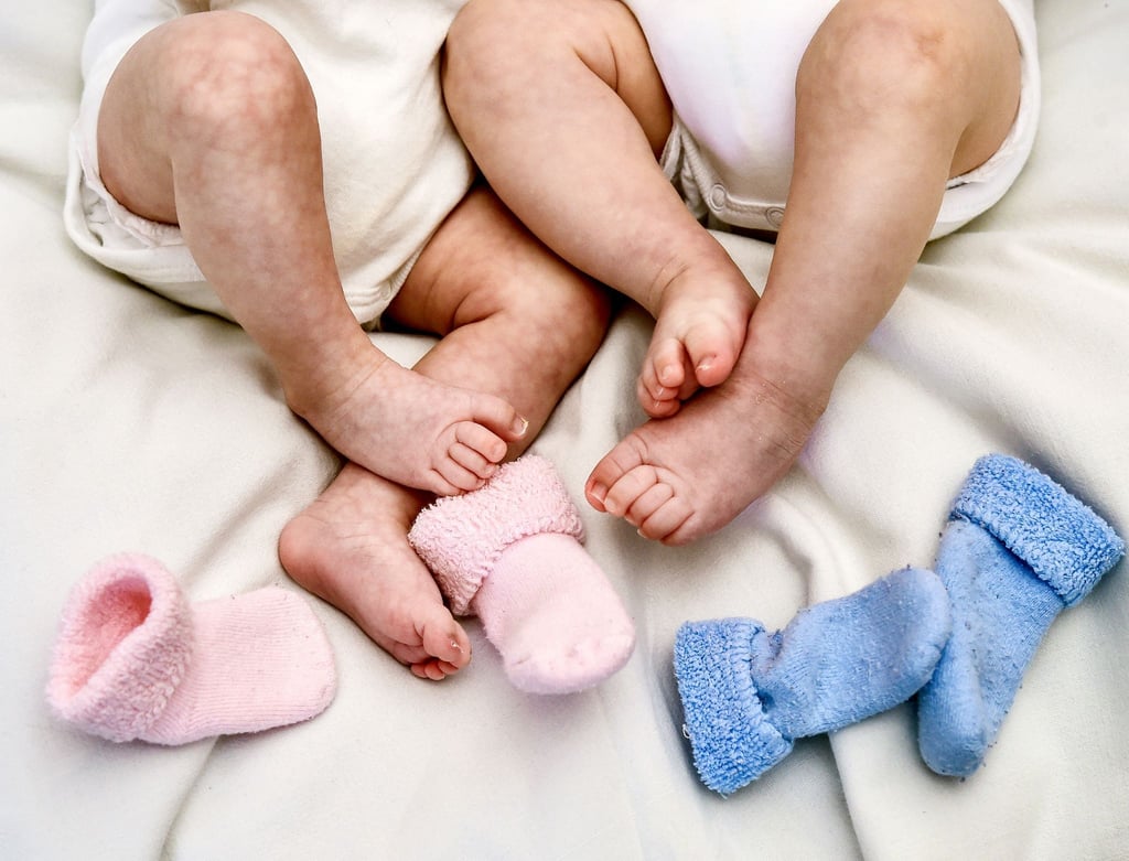 ILLUSTRATION - Rosa und blaue Söckchen für ein Mädchen und einen Jungen und die nackten Babybeine von Zwillingen.
