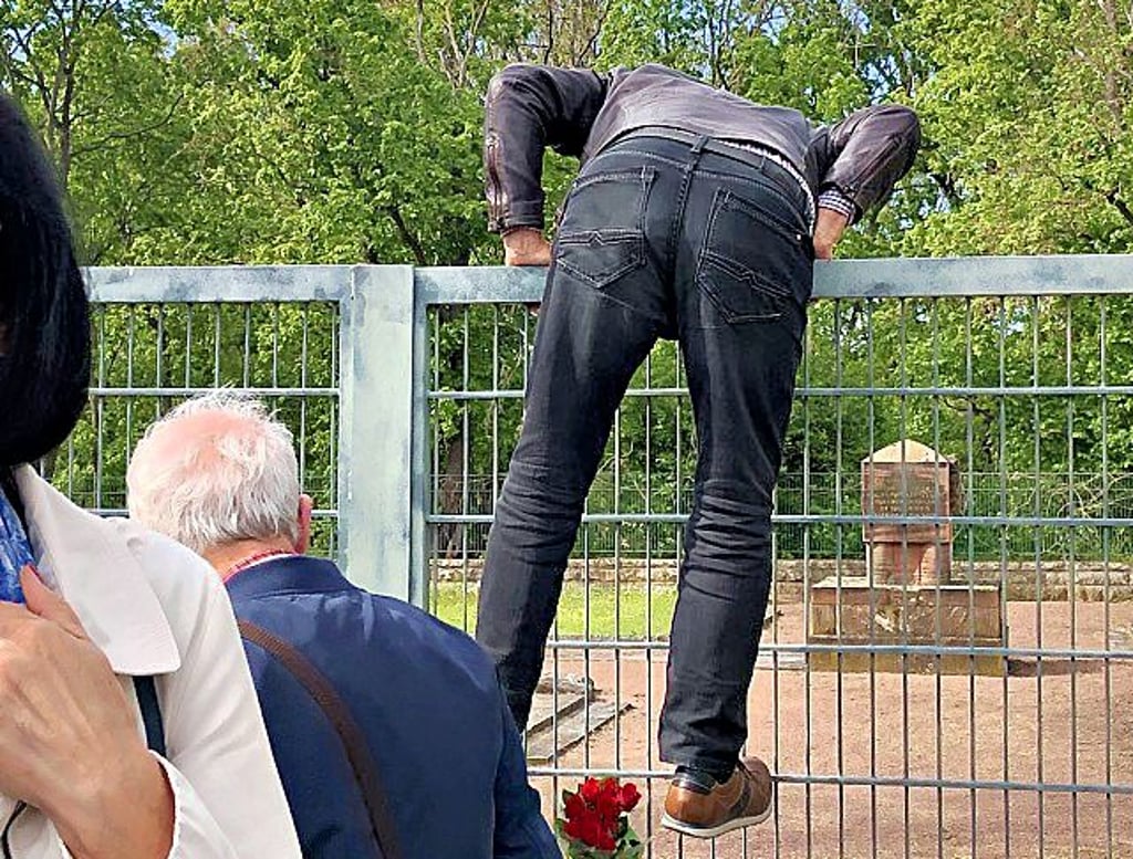 Hier versucht ein Teilnehmer der Gedenkveranstaltung sogar, über den Zaun zu klettern.