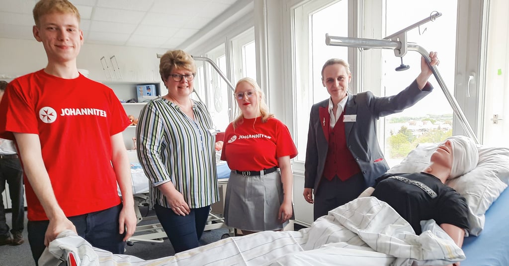 Die Pflegeschüler Hannes Barysch und Leonie Holz stehen gemeinsam mit Pflegeschulleiterin Diana Maurer (rechts) und Kursleiterin Beate Sydow-Guttek vor einem Übungskrankenbett mit der Puppe "Herbert".