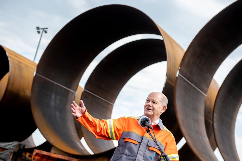 Bundeskanzler Olaf Scholz (SPD) steht vor Bauteilen für die Stahlfundamente von Windkraftanlagen.