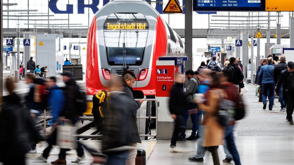 Zahlreiche Menschen gehen über einen Bahnsteig an einem Bahnhof.